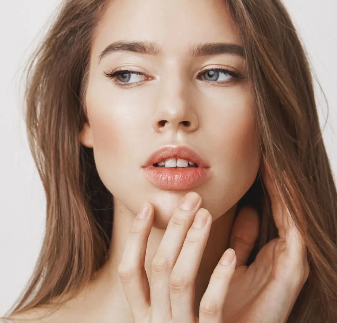 Woman with brown hair touching her chin against a neutral background